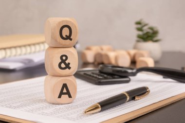 Finans belgelerinde soru ve cevapları sembolize eden soru ve cevapları gösteren tahta bloklar yığını. arka planda kalem, hesap makinesi ve ofis aksesuarları profesyonel bir ayar oluşturur