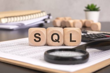 Bu resim SQL veritabanı yönetimini ve veri analizini temsil ediyor. SQL içeren tahta küplerin yanında bir büyüteç, bir hesap makinesi ve ofis gereçleri, veri odaklı karar verme mekanizmasını sembolize ediyor.