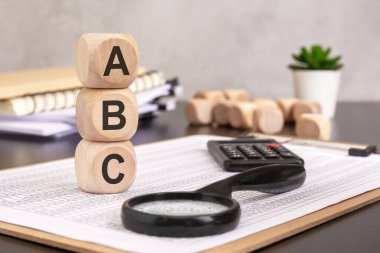 Görüntü temel, öğrenme ve organizasyonu sembolize eder. 'ABC' yi heceleyen tahta bloklar finansal belgelere, bir büyüteç, hesap makinesi ve ofis ögeleri ile yerleştirilmiş, analizi ve yapılandırılmış verileri temsil etmektedir.