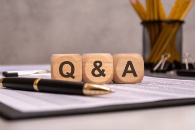 Kalem, dizüstü bilgisayar ve ofis malzemeleri eşliğinde 'Q ve A' iş belgeleriyle ahşap bloklar. Müşteri desteği, iş iletişimi, kurumsal toplantılar, FAQ 'lar ve profesyonel tartışmaları temsil eder