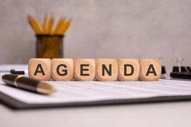 Ahşap blokta kalem, kalem ve beyaz kağıt dökümanlarıyla AGENDA sözcüğü.