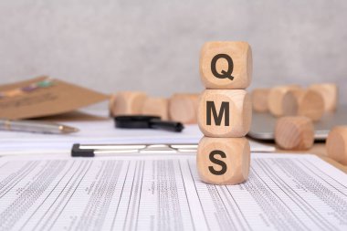 Ofis malzemelerinin, hesap çizelgelerinin ve belgelerin arka planında kısaltma oluşturan harflerle dolu tahta bloklar. İçerik kalitesi yönetim sistemi için ideal