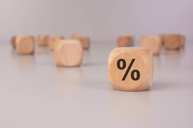 Keskin odak noktasında yüzde işareti olan tahta bir küp. Arka plandaki bulanık tahta bloklar bankacılık, faiz oranları ve ekonomiyle ilgili minimalist bir finansal konsept oluşturur.