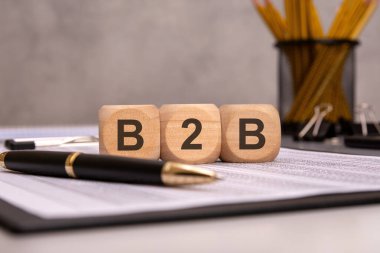 İş belgelerinde 'B2B' yazan tahta bloklar, yanında kalem, dizüstü bilgisayar ve ofis malzemeleri var. Müşteri desteği, iş iletişimi ve profesyonel tartışmaları temsil eder
