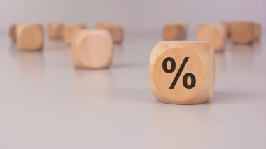 Keskin odak noktasında yüzde işareti olan tahta bir küp. Arka plandaki bulanık tahta bloklar bankacılık, faiz oranları ve ekonomiyle ilgili minimalist bir finansal konsept oluşturur.