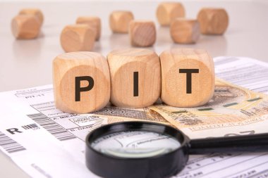 Gelir vergisi formlarında PIT 'yi oluşturan tahta küpler, büyüteç ve parayla, vergi dosyalama, mali analiz ve kişisel gelir vergilendirmesini temsil ediyor