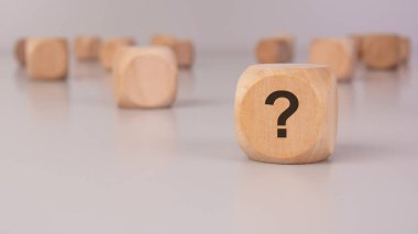 Arkaplanda bulanık küplerle çevrili, üzerinde bir soru işareti olan tahta blok. Belirsizlik, karar verme, problem çözme ve iş ve hayatta çözümler bulma