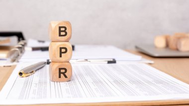 wooden cubes forming BPR on financial reports, with pens and a laptop in the background, representing business process reengineering, corporate strategy, and workflow optimization clipart