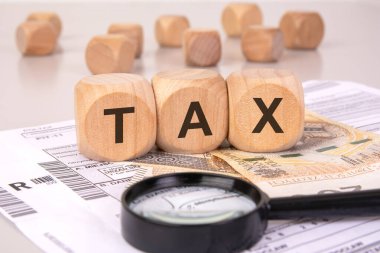 Gelir vergisi formlarında vergi oluşturan tahta küpler, büyüteç ve parayla vergi dosyalarını, finansal analizleri ve kişisel gelir vergilerini temsil ediyor.