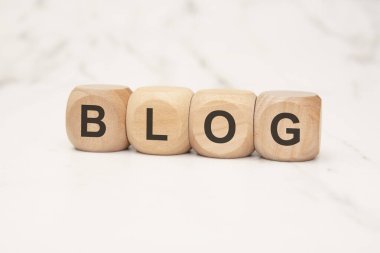 Dört tahta küp koyu siyah harflerle açık mermer yüzeyde BLOG yazılıyor. resim blog yazma, dijital içerik oluşturma ve çevrimiçi yayınlamayı modern ve minimalist bir tarzda temsil eder.