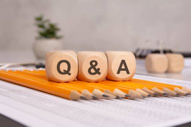 Q ve A harflerinin yer aldığı tahta küpleri ofis belgelerinin üzerine yerleştirilmiş kalemlerin üzerine yerleştirilmiş. Bu resim soruları ve cevapları, iletişimi, eğitimi ve tartışmayı temsil eder..
