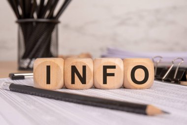 Finansal belgelerde INFO kelimesini oluşturan dört tahta blok, iş verilerini, bilgilerini ve analizlerini temsil ediyor. Kalemler, klasörler ve arka plandaki kağıtlar gibi ofis unsurları profesyonel temayı geliştirir.