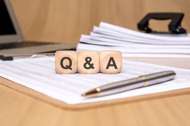 Finansal tablolarda Q ve A 'yı gösteren üç tahta küp ve arka planda da bir kalem ve ofis belgeleri var. Tartışmayı, FAQ 'ları, iş danışmanlığını ve bilgi alışverişini temsil eder