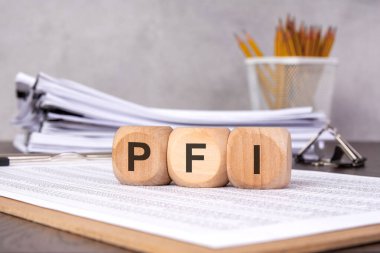 Finans tablolarına yerleştirilmiş, arka planda ofis malzemelerini gösteren üç tahta küp. Özel Finans Girişimi, kamu-özel ortaklıkları ve altyapı yatırımlarını temsil eder.