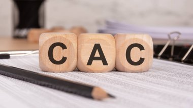 Finansal belgelere yerleştirilmiş üç tahta küp, müşteri edinme maliyetini sembolize ediyor, iş, pazarlama ve satış performans değerlendirmelerinde önemli bir ölçü