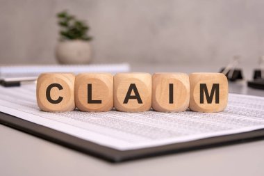 CLAIM sözcüğünün yazılı olduğu tahta küpler, sigorta, yasal ya da finansal talepleri temsil eden evrak işleri üzerinde dinleniyor. arka planda ofis malzemeleri, profesyonel bir ortam oluşturuluyor
