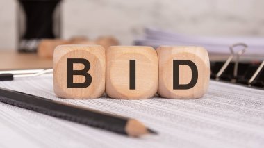 Finansal belgelere BID harfleri iliştirilmiş üç tahta blok. Ofis malzemeleri arka planda. Müzayede, yatırım, ticari işlemler ve ekonomik strateji kavramı