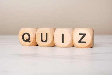 Tarafsız bir yüzey üzerinde QUIZ kelimesini oluşturan dört tahta küp, eğitim, bilgi ve ıvır zıvır kavramlarını temsil ediyor, sınavlar, testler ve öğrenme temaları için ideal.