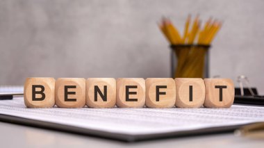 BENEFIT sözcüğünü oluşturan tahta bloklar finansal tablolara yerleştirildi. Arka planda ofis malzemeleri, finansal ve ticari büyümenin vurgulanması, avantajlar ve karlılık kavramları yer alıyor.