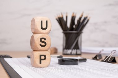 USP harfli üç tahta küp. Finansal belgelerde dikey olarak istiflenmiş. Bir büyüteç, bir tutacağa siyah kalemler ve bir masaya dizilmiş klasör benzersiz satış önerisi ve iş stratejisini sembolize ediyor..