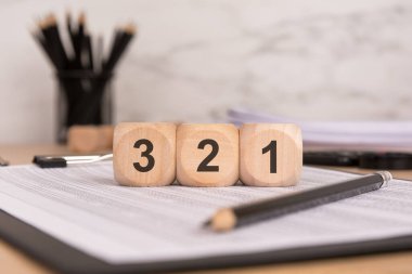 Finansal belgelerde 3, 2, 1 rakamlarını gösteren üç tahta küp bir geri sayımı ya da harekete hazırlanmayı temsil ediyor. bir siyah kalem, cilt klipleri ve ofis malzemeleri profesyonel bir çalışma ortamı oluşturur