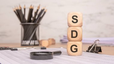 Sürdürülebilir Kalkınma Hedeflerini, belge ve araçlarla ofis ortamını sembolize eden bir masanın üzerindeki SDG tahta bloklar