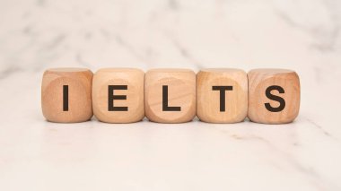 Tahta küplerdeki IELTS kısaltması, beyaz mermer bir yüzey üzerindeki dil yeterlilik sınavlarını sembolize ediyor