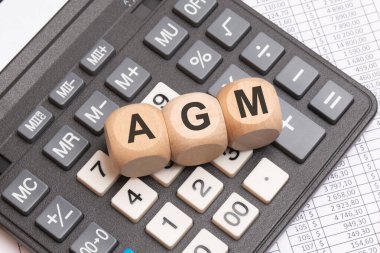 AGM sözcüğü - Yıllık Genel Kurul - hesap makinesinde ahşap bloklarla gösterilir, hesap tablolarıyla çevrilidir. iş toplantıları, finans ve kurumsal yönetim.