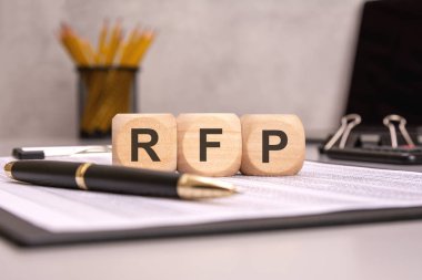 Finansal dökümanlar ve kalem içeren bir ofis masasında RFP (Teklif Talebi) içeren tahta bloklar.