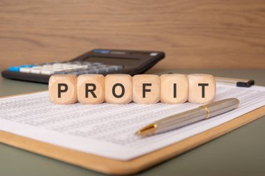 PROFIT kelimesi arkaplanda kalem ve hesap makinesi olan bir hesap tablosuna yerleştirilmiş tahta bloklar kullanılarak yazıldı. İş geliri, kazanç ya da mali başarı kavramı.