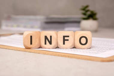 INFO 'yu heceleyen siyah büyük harfli dört yuvarlak tahta küp içinde mali belge bulunan bir panoya yerleştirildi. Bulanık bir ofis arkaplanı ve saksı bitkisi içeriği ekler.