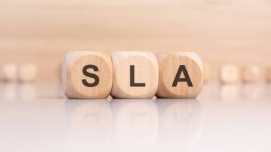 Kısaltması SLA Hizmet Seviyesi Anlaşması olan üç tahta küp parlak bir yansıtıcı yüzeyde, iş terimleri ve bilişim hizmetlerini temsil eden yumuşak nötr bir arkaplan ile sıralanmış..