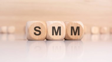 Yansıtıcı bir yüzeyde SMM yazılı üç tahta küp, sosyal medya pazarlama stratejisini ve dijital promosyonu sembolize ediyor.