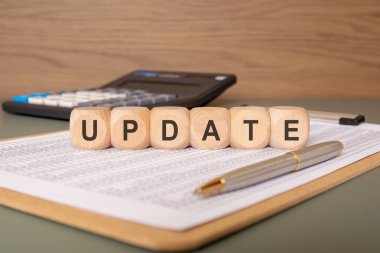 UPDATE 'in finansal tabloya yerleştirildiği ahşap blokların yakın plan görüntüsü. Arka planda veri incelemesini veya belge revizyonunu sembolize eden gümüş bir kalem ve bir hesap makinesi görünür.