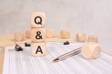 Hesap tablosunda soru-cevap harflerini gösteren üç tahta küpten oluşan dikey yığın. Masanın üzerinde gümüş bir kalem ve ataç var. arkaplan daha fazla tahta blok içeriyor.