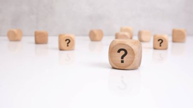 Üzerinde siyah bir soru işareti olan tek bir tahta blok beyaz parlak bir masaya odaklanır. Bu, iş ya da hayattaki karmaşayı, soruşturmayı, şüpheyi ya da karar verme mekanizmasını sembolize eder..