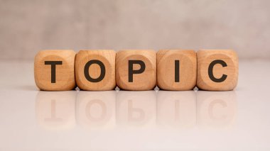 Tahta bloklar yansıtıcı yüzeyde TOPIC kelimesini oluşturuyor. Konu, tema, tartışma, sohbet, eğitim veya iş sunumu kavramı.
