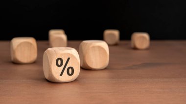 Doğal ahşap bloğa yakın plan. Kahverengi masada siyah yüzde sembolü, dağınık küpleri ve koyu arkaplanı var. Mali faiz oranlarını temsil eden indirim veya ekonomik büyüme kavramı