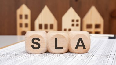 Arka planda ahşap ev modelleri, hizmet düzeyi anlaşmasını ve iş yönetimi kavramlarını sembolize eden SLA 'nın kısaltması olan tahtadan küpler.
