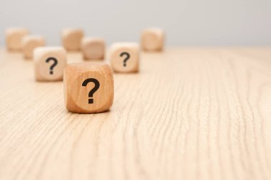 a natural wooden block printed with question mark sits sharply in the foreground on a wooden desk, while other cubes blur in the background. symbolizes uncertainty, inquiry, decision-making, questions.