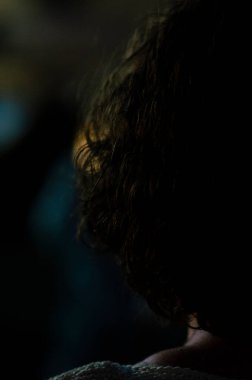 Karanlık dramatik aydınlatma, yalnızlık ve tefekküre dalmış kıvırcık saçlı gizemli bir insan silueti.