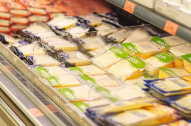 Çeşitli dilimlenmiş Gouda peyniri paketleri modern bir süpermarkette soğutulmuş bir rafta, süt ürünleri bölümünde çeşitlilik ve tazelik sergileniyor..