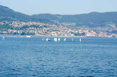 Sakin mavi sularda küçük yelkenli teknelerin manzarası, canlı bir kıyı kenti ve bereketli bir dağ manzarası, boş zamanları ve yaz maceralarını çağrıştırıyor..