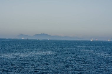 Sakin bir yelkenli sahnesi. Arka planda sisli dağlar olan sakin mavi bir denizde süzülüyor. Yaz, seyahat ve deniz temaları için mükemmel..