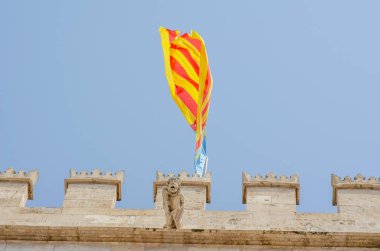 Geleneksel Valencia bayrağı, İspanya Valencia 'nın ikonik mimarisini ve canlı kültürünü yakalayan aslan heykeli ile tarihi taş siperlerin üzerinde dalgalanıyor..
