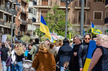 Ukrayna bayrakları ve protesto işaretleri sallayan, halka açık bir gösteri sırasında Ukrayna 'ya ve barışa destek veren büyük bir grup insan bir şehir caddesinde toplanıyor..