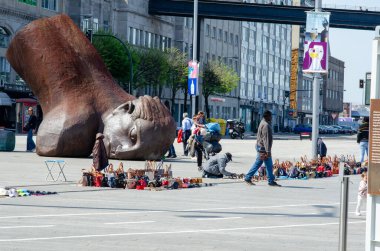 Hayat dolu bir Avrupa şehir meydanında modern bir sanat başlığı heykelinin yanında çanta ve aksesuar satan sokak satıcılarını gösteren canlı şehir manzarası..