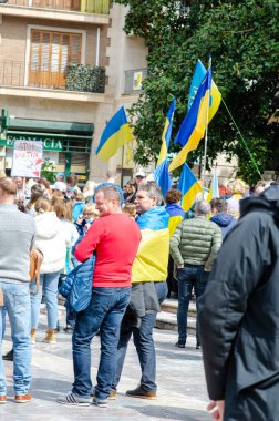 Bir grup insan Ukrayna bayrakları taşıyan şehir meydanında toplanarak özgürlük ve savaşa karşı barışçıl bir gösteri yapıyor. Protesto atmosferi, sivil aktivizm.