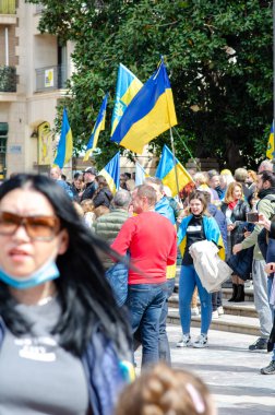 Ukrayna 'yı destekleyen, elinde ulusal bayraklar tutan ve güneşli bir şehir ortamında dayanışma gösteren canlı bir halk gösterisi. Protestolar ve sivil birlik üzerine makale içeriği için mükemmel.