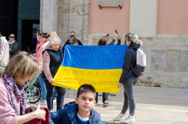 İnsanlar, Ukrayna bayrağıyla güneşli bir Avrupa şehir meydanında toplanarak Ukrayna ile dayanışma ve destek çağrısı yapıyorlar..